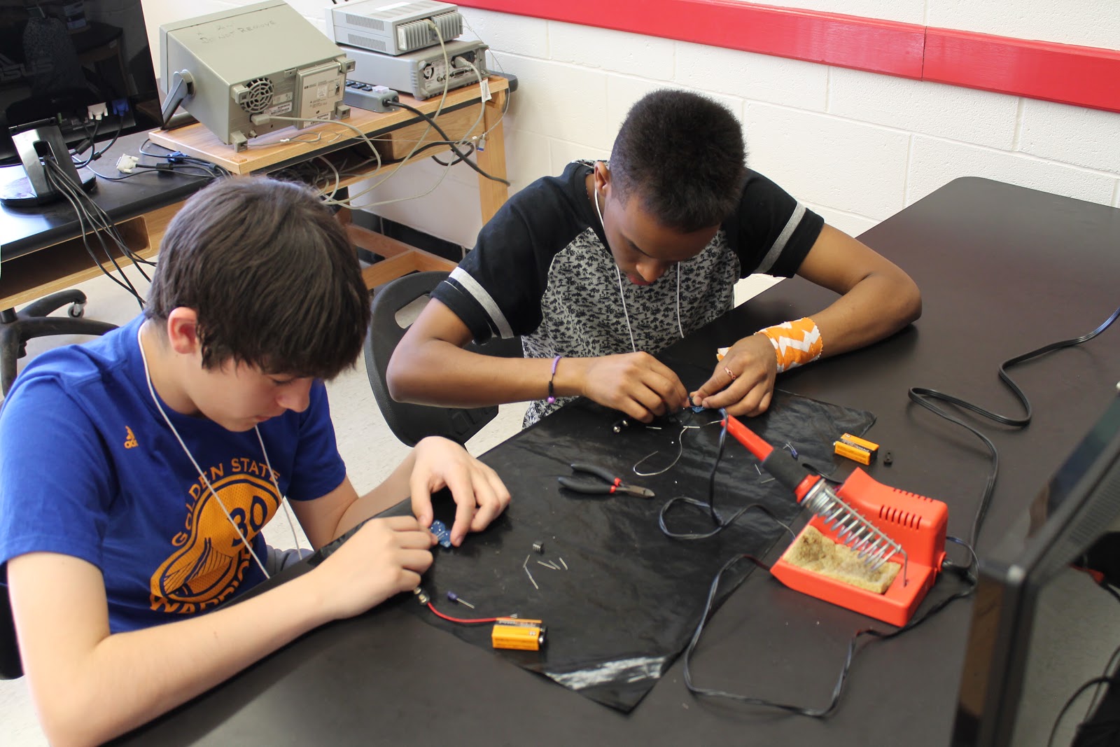 two teenagers building electronics at a table
