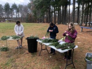 three girls making holiday wreaths with fresh branches