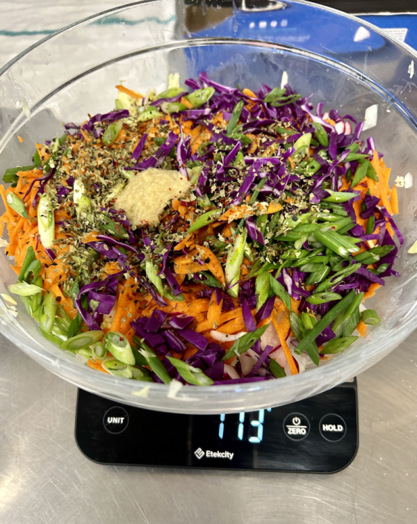 Glass bowl filled with shredded purple cabbage, green onions, carrots, and spices on a digital scale