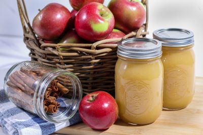 A basket of apples alongside home-canned applesauce and a jar with cinnamon sticks.