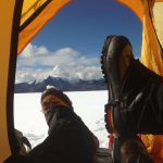 View of researchers' feet as they rest in their tent and look out across the ice sheet at the mountain range beyond