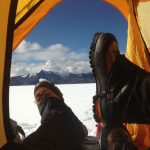 View of researchers' feet as they rest in their tent and look out across the ice sheet at the mountain range beyond