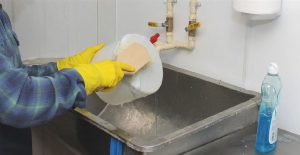 cheesemaker cleans equipment with soap and brush