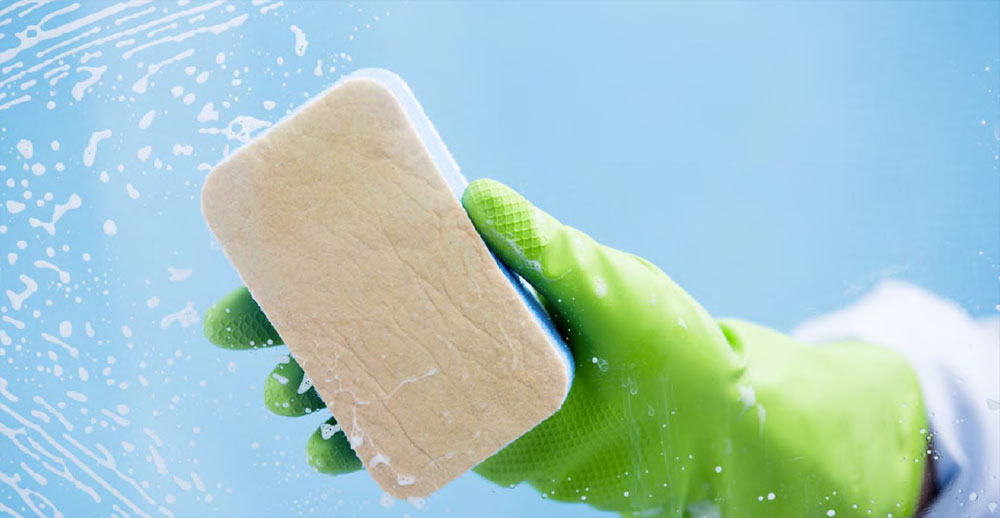 Person wearing rubber gloves holding a soapy sponge