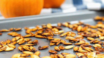 Roasted pumpkin seeds on a baking sheet with pumpkins in the background