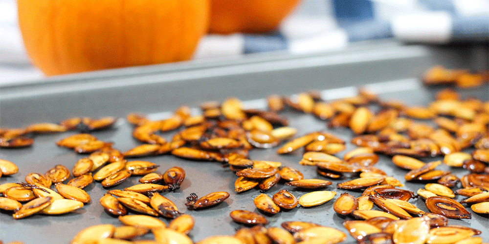 Roasted pumpkin seeds on a baking sheet with pumpkins in the background