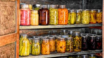 several rows of home canned food in glass jars on shelves in a wooden cabinet