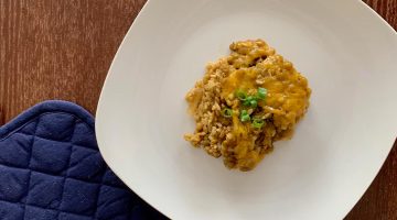Cheesy Lentil Casserole on a square white plate with a blue pot holder on the side