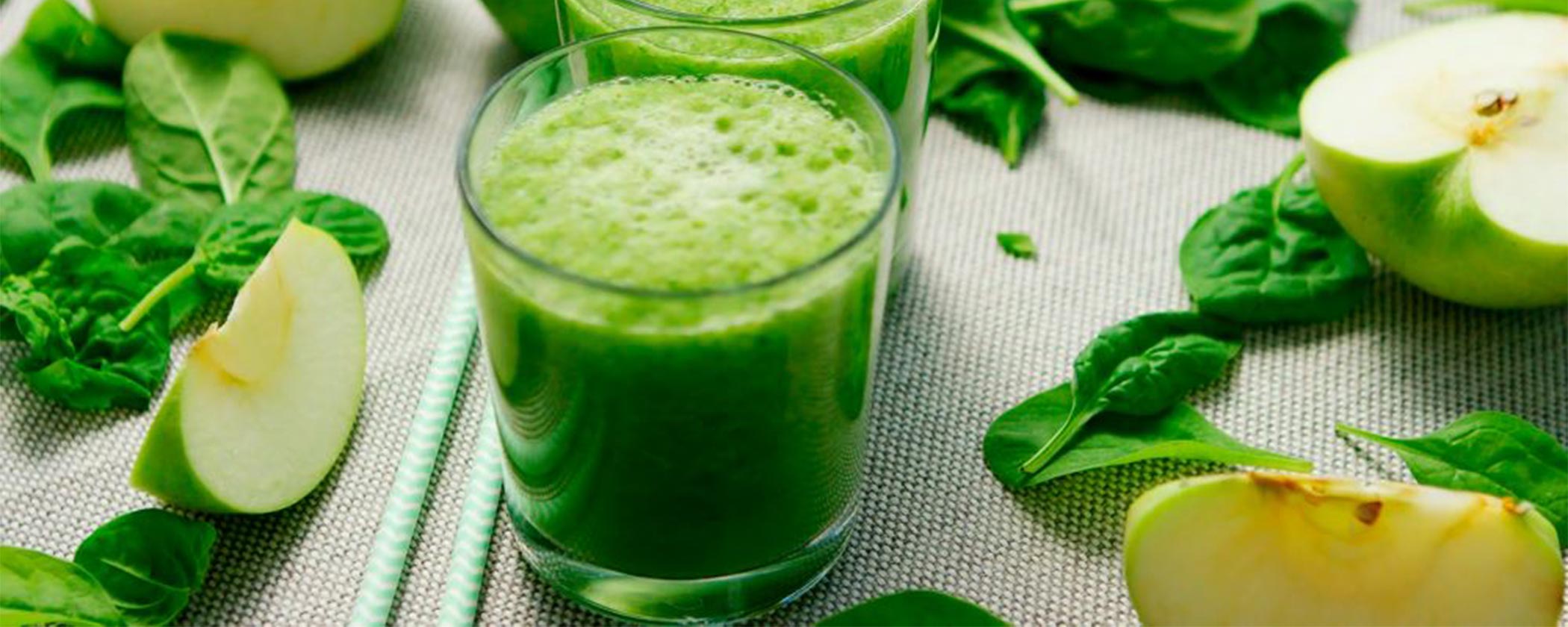 Green smoothie in clear glasses with spinach leaves and green apples on table