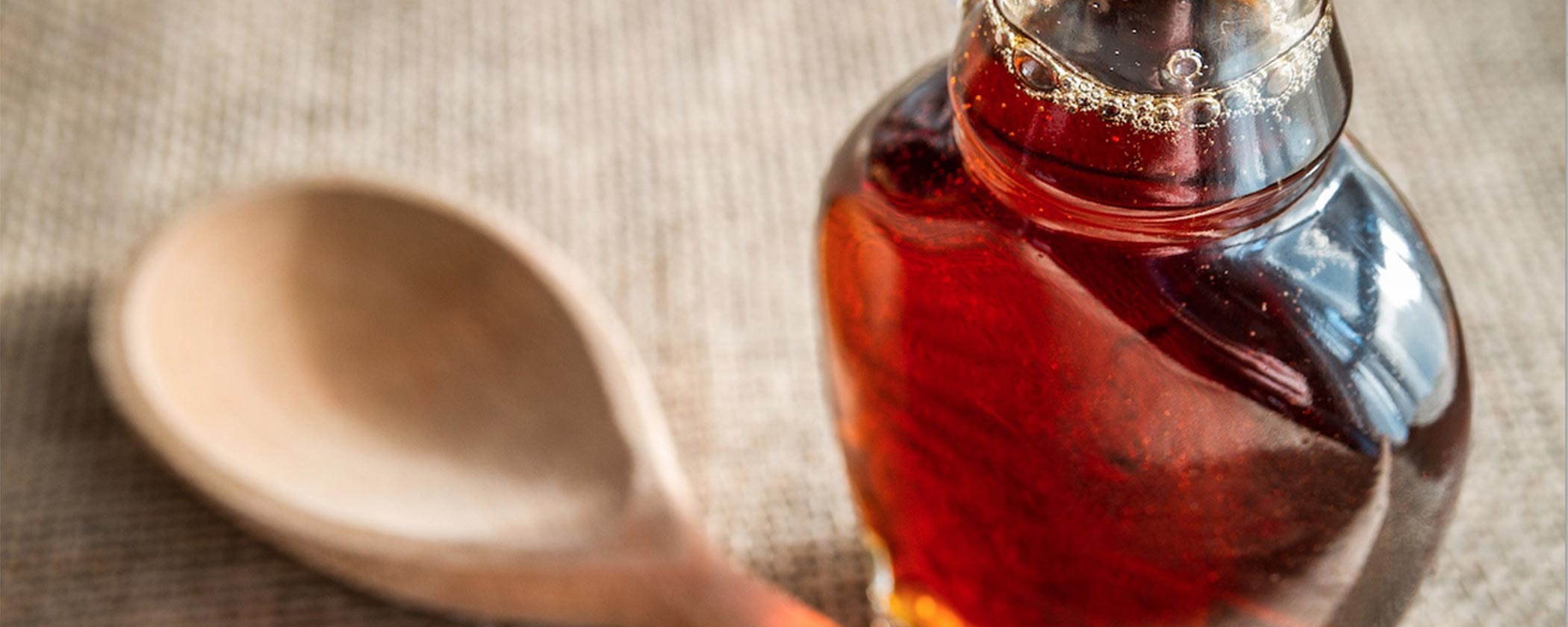 wooden spoon next to a glass bottle of amber maple syrup