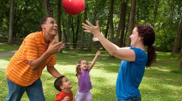 Parents with two young children play outside with a handball.