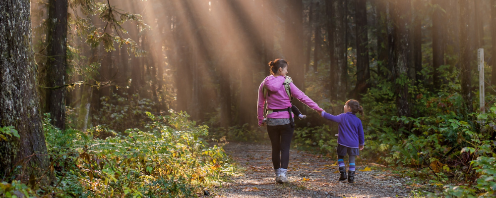 Sun rays beaming down on mother and daughter walking in a forest
