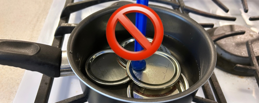 Canning jar lids in a pan on a stove with a red circle with a line through it.