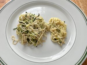 Two piles of zoodles on a plate. One is in a tight pile and the other pile is looser..