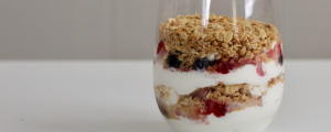 Yogurt fruit parfait with granola, strawberries, blueberries, and yogurt in a clear glass on a table.