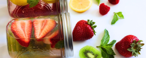 Flavored water in mason jars with strawberries, kiwi, lemon, raspberries, and mint leaves.