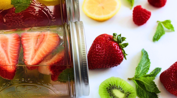 Flavored water in mason jars with strawberries, kiwi, lemon, raspberries, and mint leaves.
