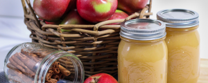 Canned apple sauce with cinnamon sticks and a basket of apples.