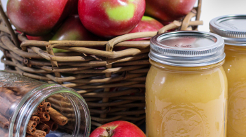 Canned apple sauce with cinnamon sticks and a basket of apples.