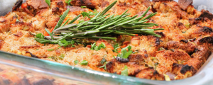 Cooked stuffing in a glass baking dish with fresh rosemary sprig on top as garnish.