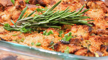 Cooked stuffing in a glass baking dish with fresh rosemary sprig on top as garnish.