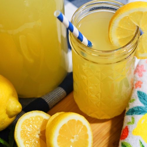glass of honey sweetened lemonade with a lemon slice next to lemons