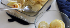 Scalloped potatoes in a glass bowl with a blue pot holder in the background.