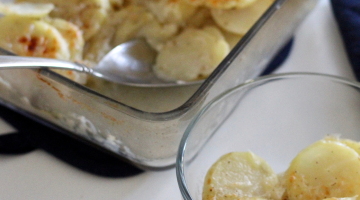 Scalloped potatoes in a glass bowl with a blue pot holder in the background.