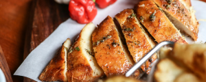 A plate of sliced, roasted chicken breast with herbs and spices.