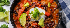 Bowl of black bean soup topped with avocado, sour cream, cilantro, and lime wedges.