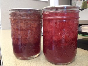 Two jars of strawberry jam with separation in the jars.