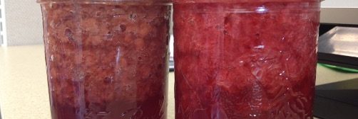 Two jars of strawberry jam with separation in the jars.