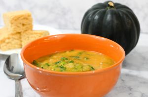 Acorn squash soup in an orange soup bowl with corn bread and a whole acorn squash in the background.