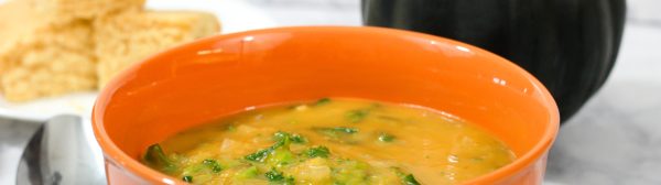 Acorn squash soup in an orange soup bowl with corn bread and a whole acorn squash in the background.