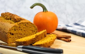 Pumpkin bread loaf sliced with mini pumpkin and cinnamon sticks in the background.