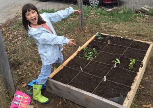 "Kids Can Grow" youth participant stands proudly next to her newly planted square-foot, raised-bed garden