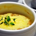 a bowl of onion soup with cheese and herb on top