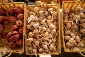 top down view of three wooden baskets. One filled with bright pink shallots, the other two filled with garlic heads. 