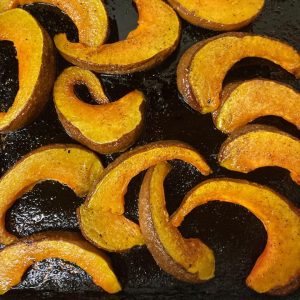 Top down view of several golden c-shaped oiled and seasoned slices of roasted squash on black pan.
