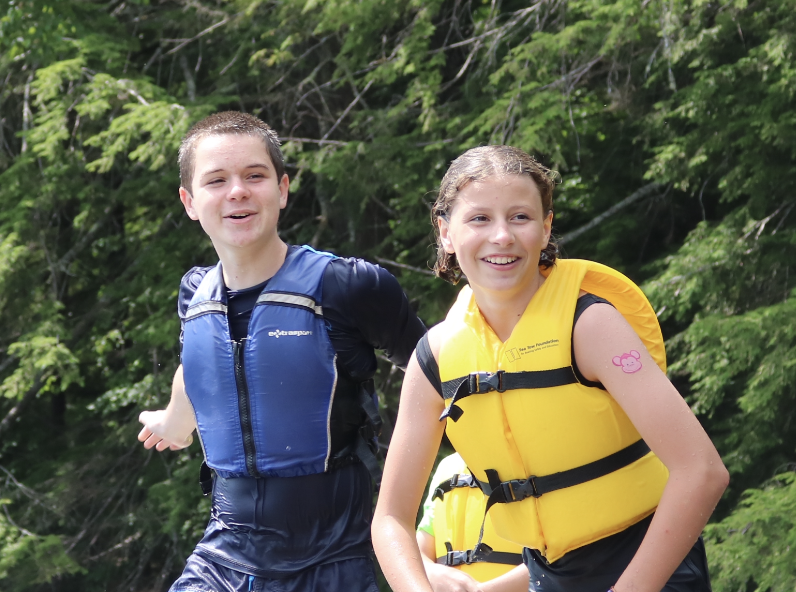 Two campers wearing lifejackets on the dock smiling