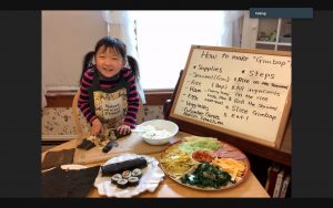 A girl giving her 4-H Public Speaking Demonstration virtually. She is surrounded by food and tools to show how to make Gimbap. 
