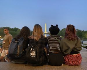 Four girls with their backs to the camera looking at the Washington monument at dusk