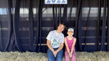 4-H Worker and Student sitting on hay bales under blue hill fair signage