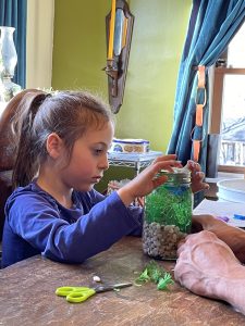 Young girl covering a decorative mason jar filled with water, fake fish, and fake plants