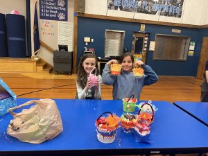 Two 4-H youth holding up their hand made may baskets in a gymnasium