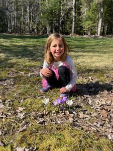 Smiling young girl behind a row of purple crocus flowers