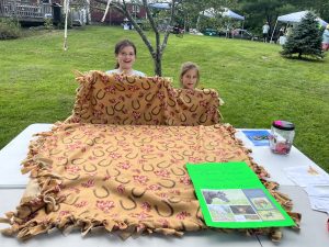 Young girls holding up a brown horse themed tie blanket with a raffle ticket sign