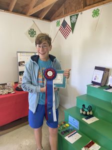 Young boy smiling widely at the camera holding up his scrapbook with a large best in show ribbon