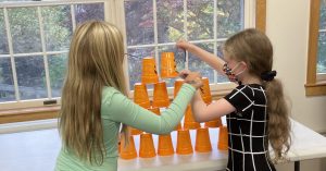Two girls building a cup tower using a rubber band and string