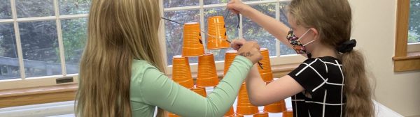 Two girls building a cup tower using a rubber band and string